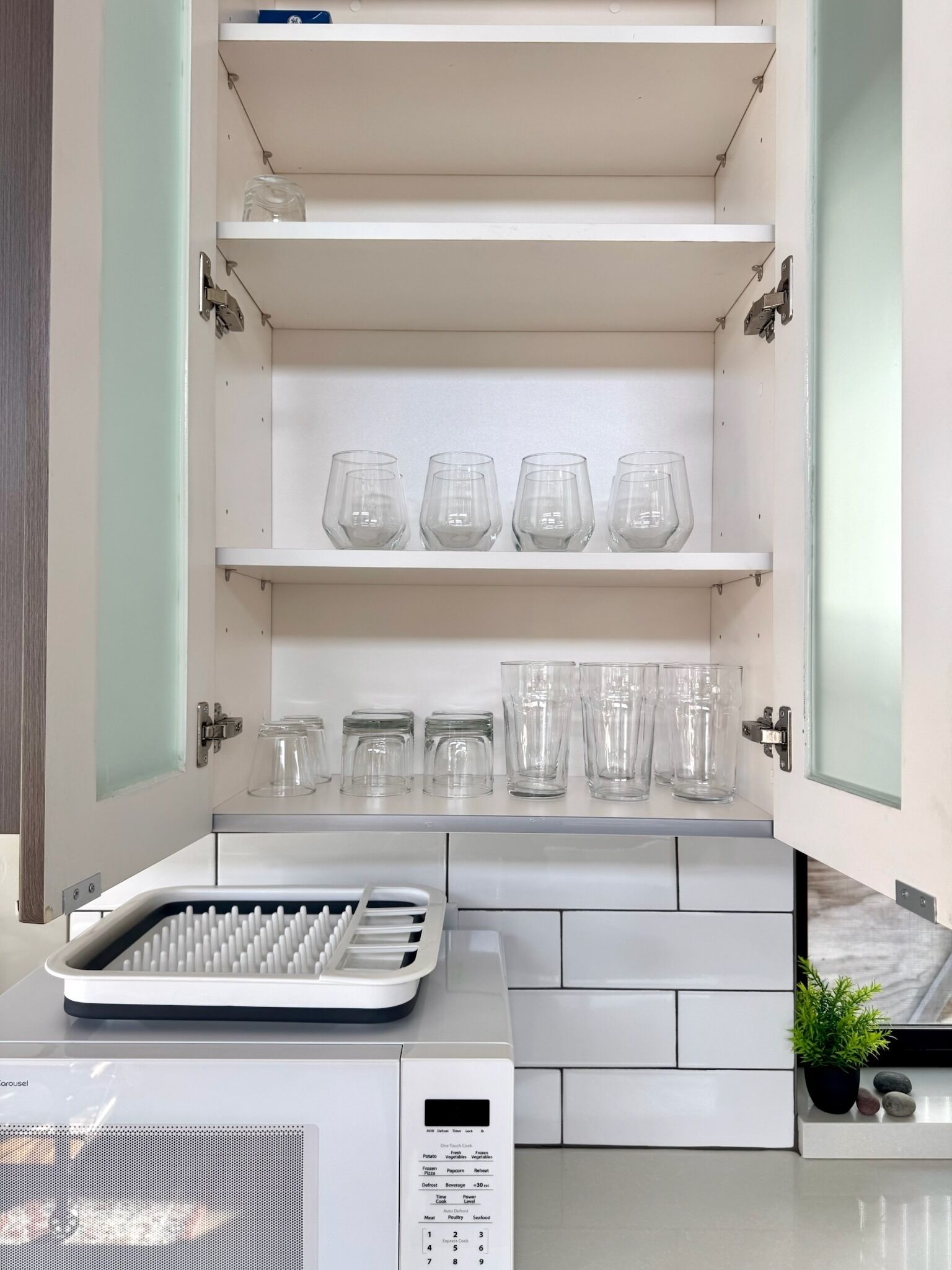 A kitchen with a microwave, a toaster, and a coffee maker. There are shelves above the counter with glassware and jars.