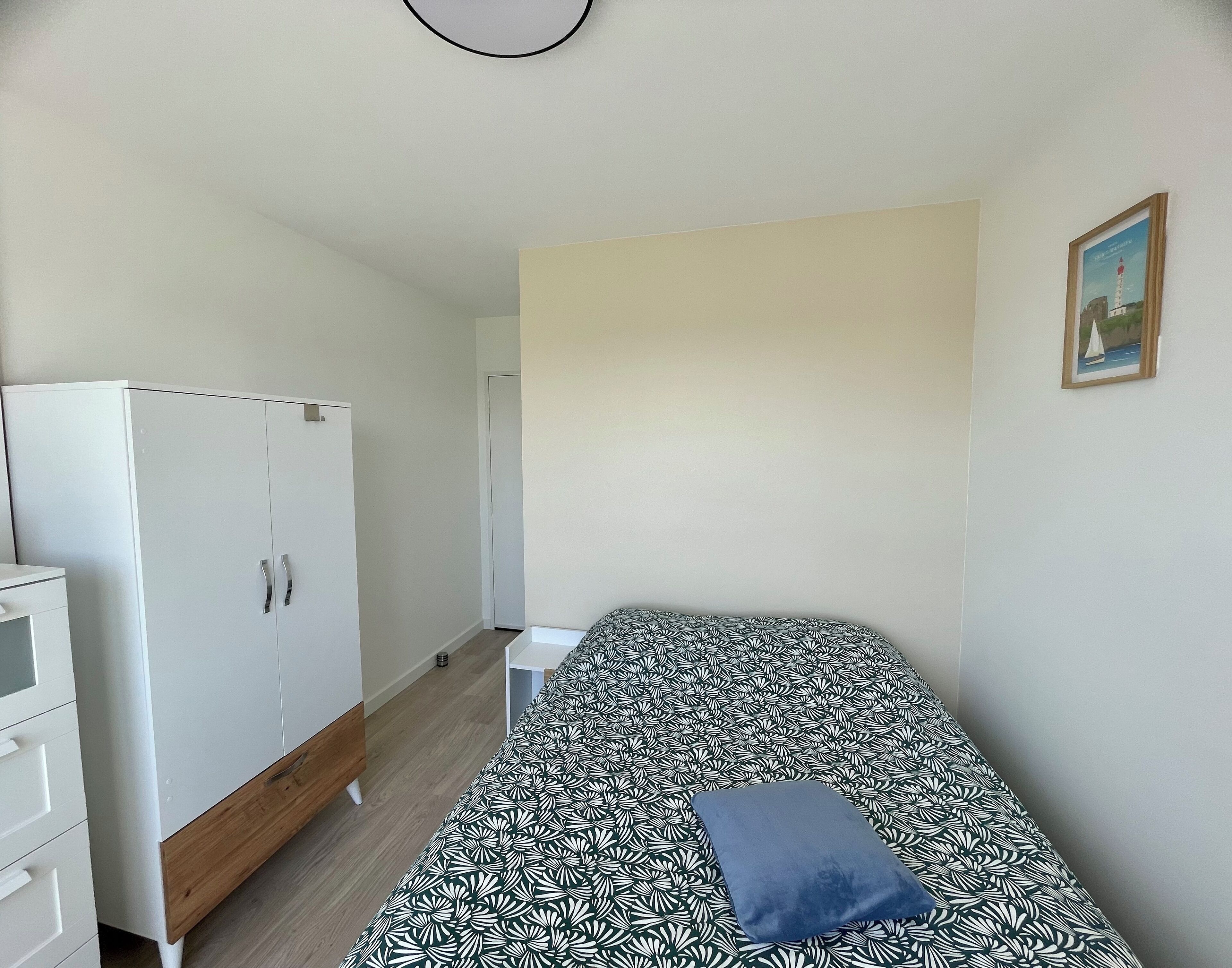 A small, sparsely furnished room with a bed, a wardrobe, and a small desk.