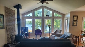 Una sala de estar con chimenea, ventanas amplias, ventilador de techo y vistas al exterior.