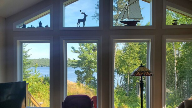 Una habitación con ventanas amplias que dan a un lago, televisión, una silla morada y una lámpara de pie.
