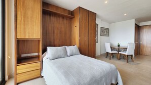 A bedroom with a bed, wooden wardrobe, and a dining area with chairs and a table. - Beautiful new Studio in Puerto Vallarta with roof top pool and ocean view (Puerto Vallarta)