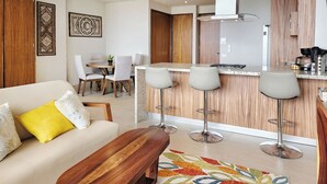 A modern living room with a sofa, a coffee table, and a dining area with chairs and a table. - Beautiful new Studio in Puerto Vallarta with roof top pool and ocean view (Puerto Vallarta)