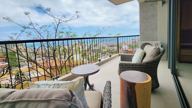 A balcony with wicker furniture, a small round table, and a view of a cityscape. - Beautiful new Studio in Puerto Vallarta with roof top pool and ocean view (Puerto Vallarta)