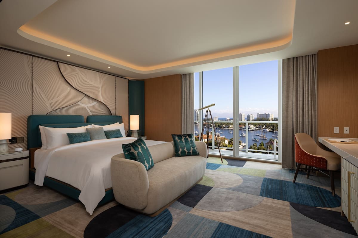 Habitación de hotel moderna con una cama grande, un sofá, un escritorio y vistas a un puerto deportivo.