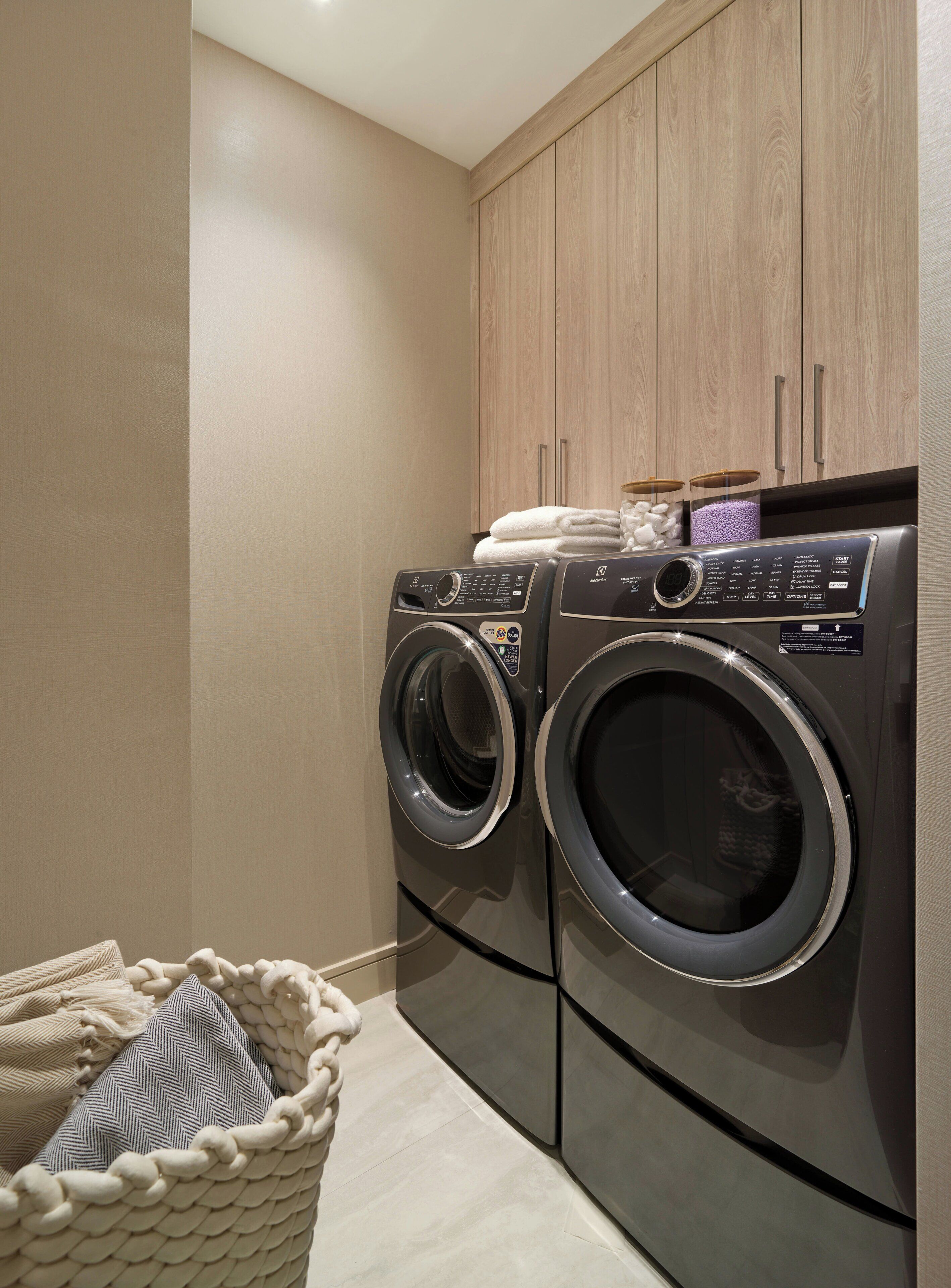A laundry area with two front-loading washing machines, wooden cabinets, and a woven basket.