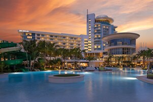 A hotel with a pool, palm trees, and a sunset sky.