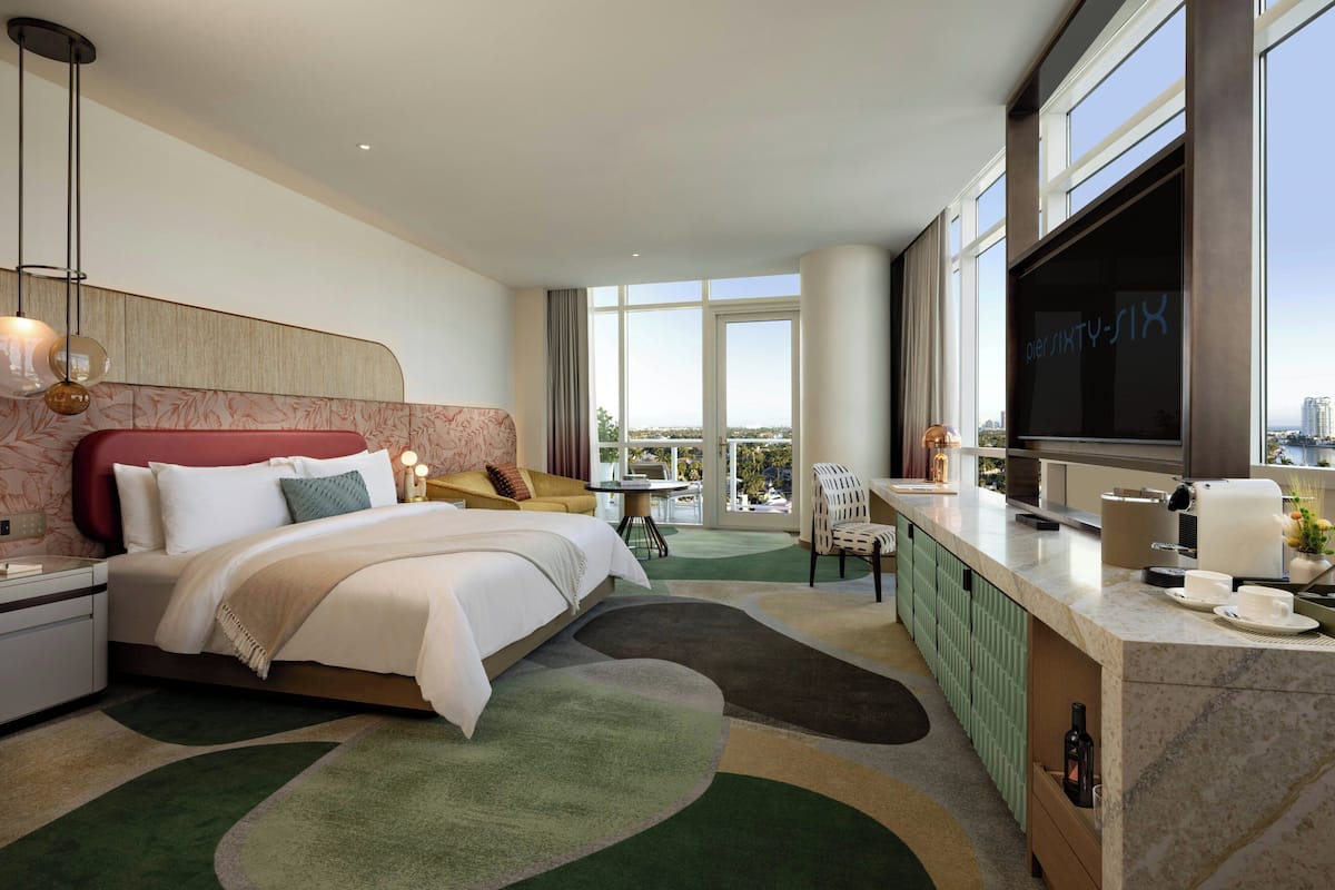 Una habitación de hotel con cama, televisor, zona de comedor y vistas a la ciudad.