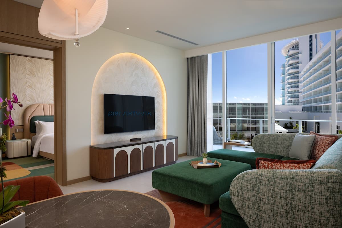 Una habitación de hotel moderna con un televisor grande, asientos tapizados en verde, una mesa de centro de mármol y vistas a un crucero.