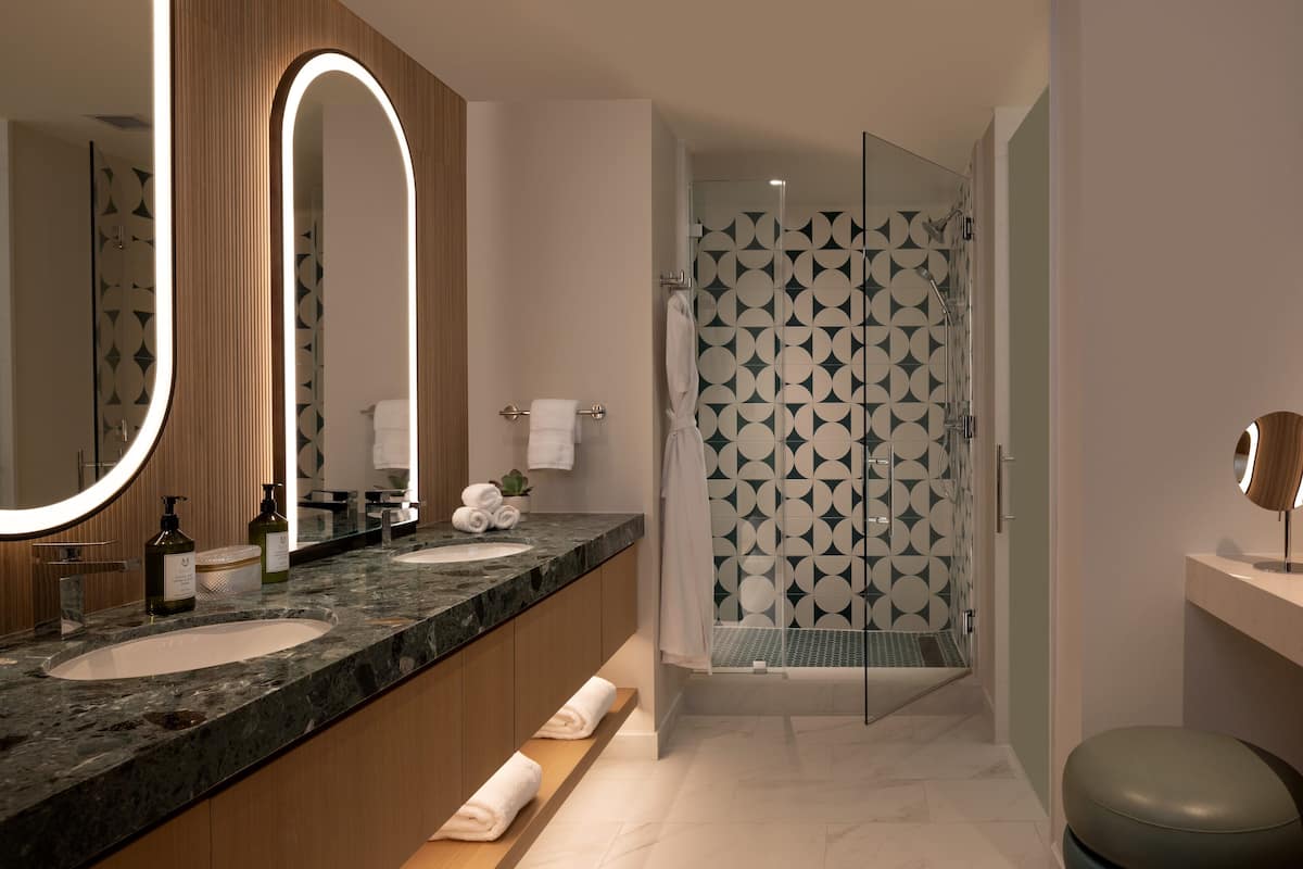 Un baño moderno con tocador de doble lavabo, un espejo grande y una ducha a ras de suelo con baldosas de patrón geométrico.
