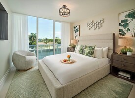 Habitación de hotel con una cama grande, una silla, una mesita de noche y vistas al exterior.