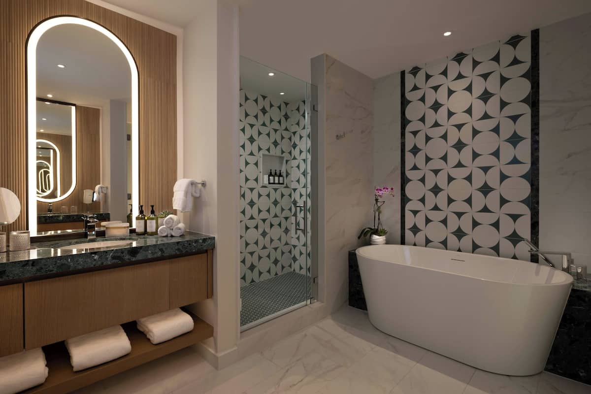 Un baño moderno con una bañera independiente, un espejo grande y un box de ducha.