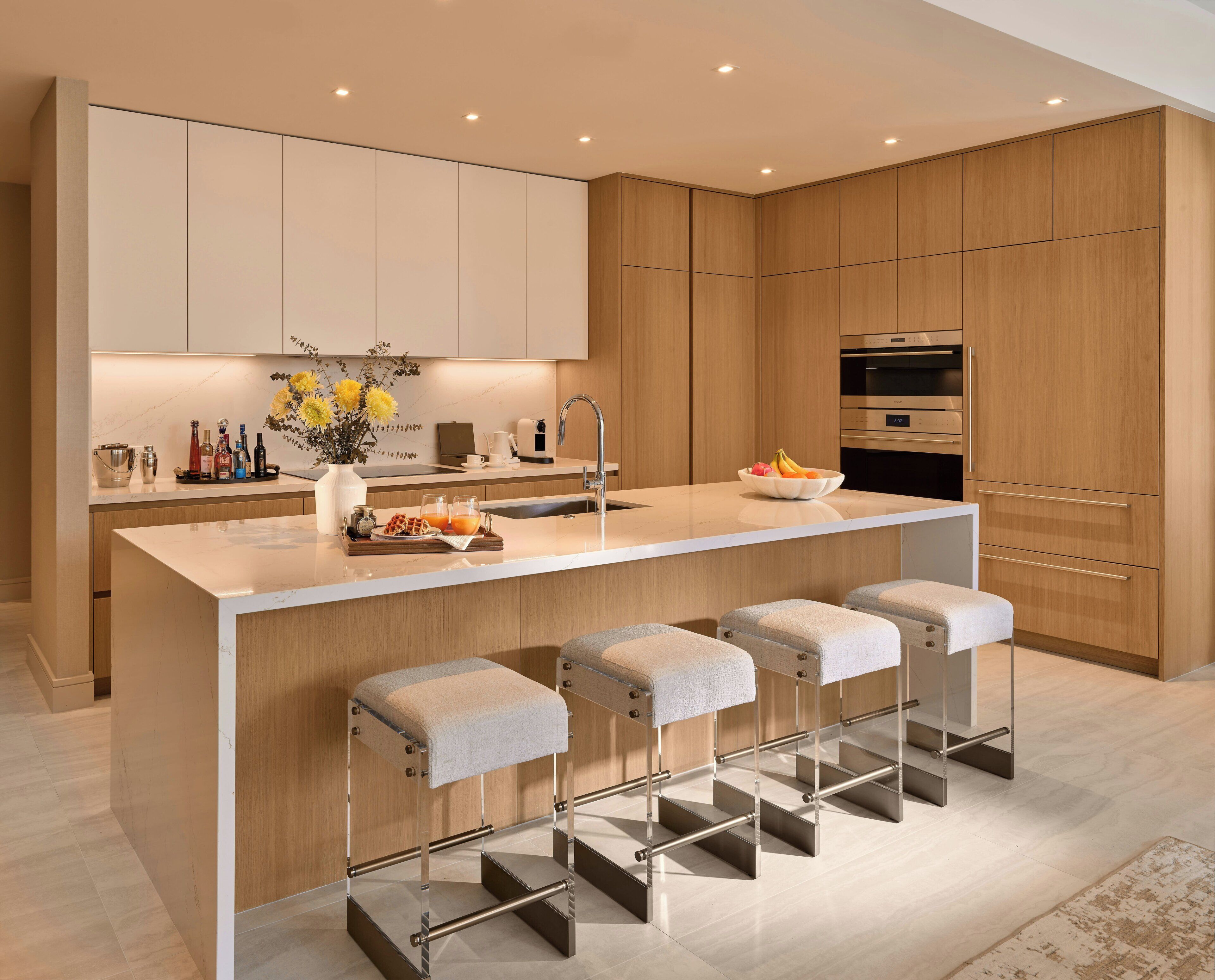 A modern kitchen with a central island, bar stools, a built-in oven, and a sink.