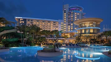 Un hotel con una amplia piscina, palmeras y un tobogán de agua.