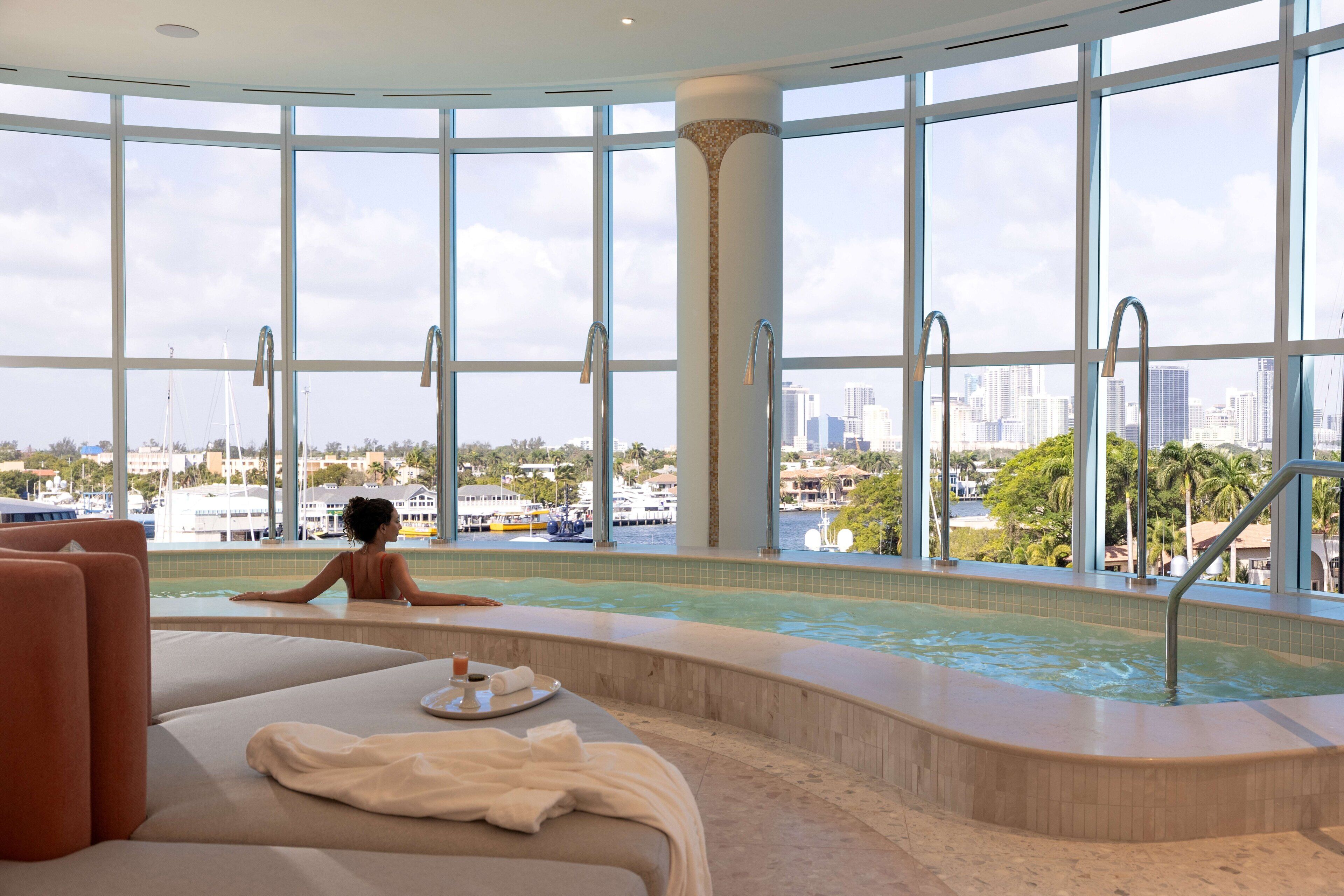 A spa area with a large window, a hot tub, and a seating area with a tray of amenities.