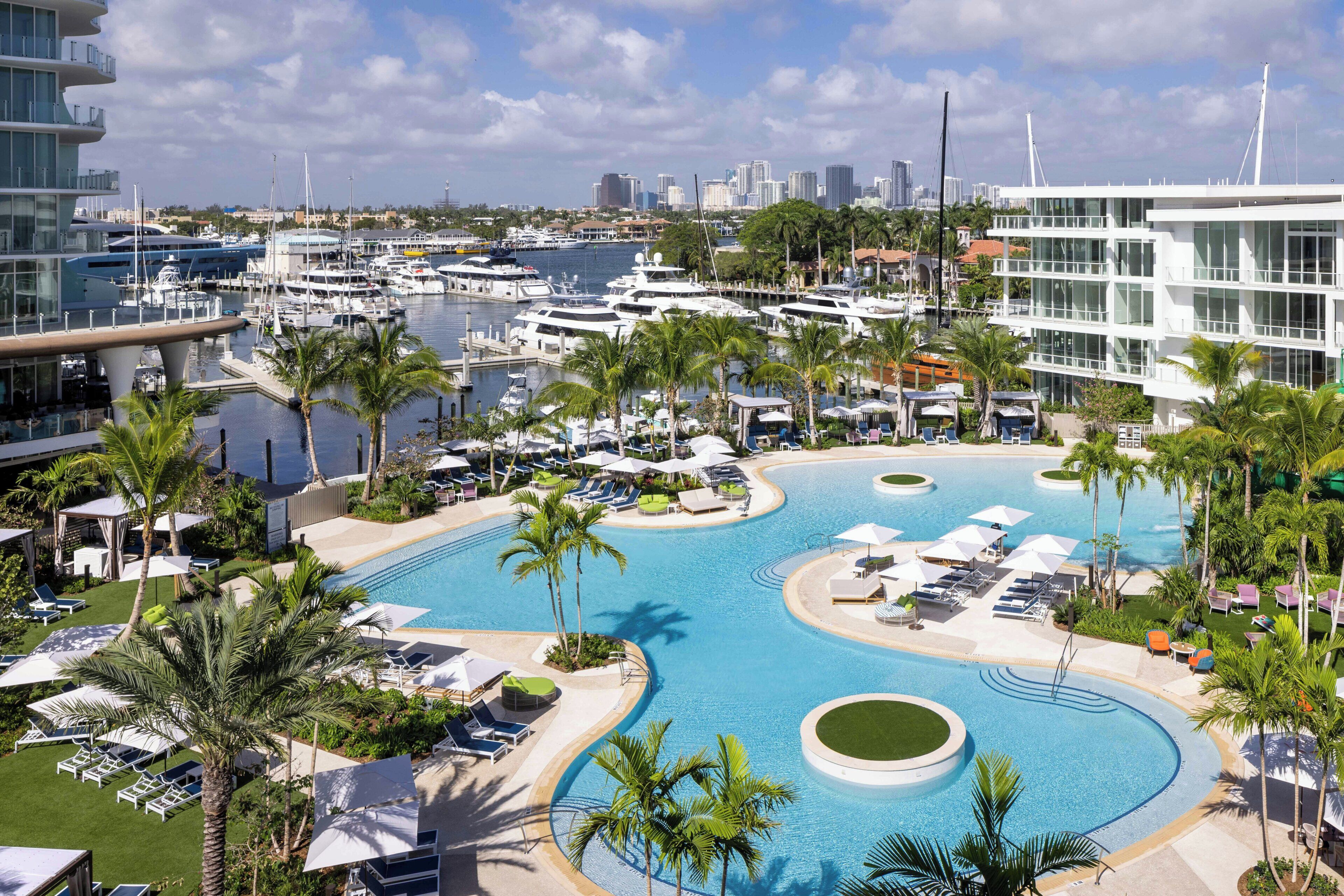A marina with boats, a swimming pool with sun loungers, and a city skyline in the background.