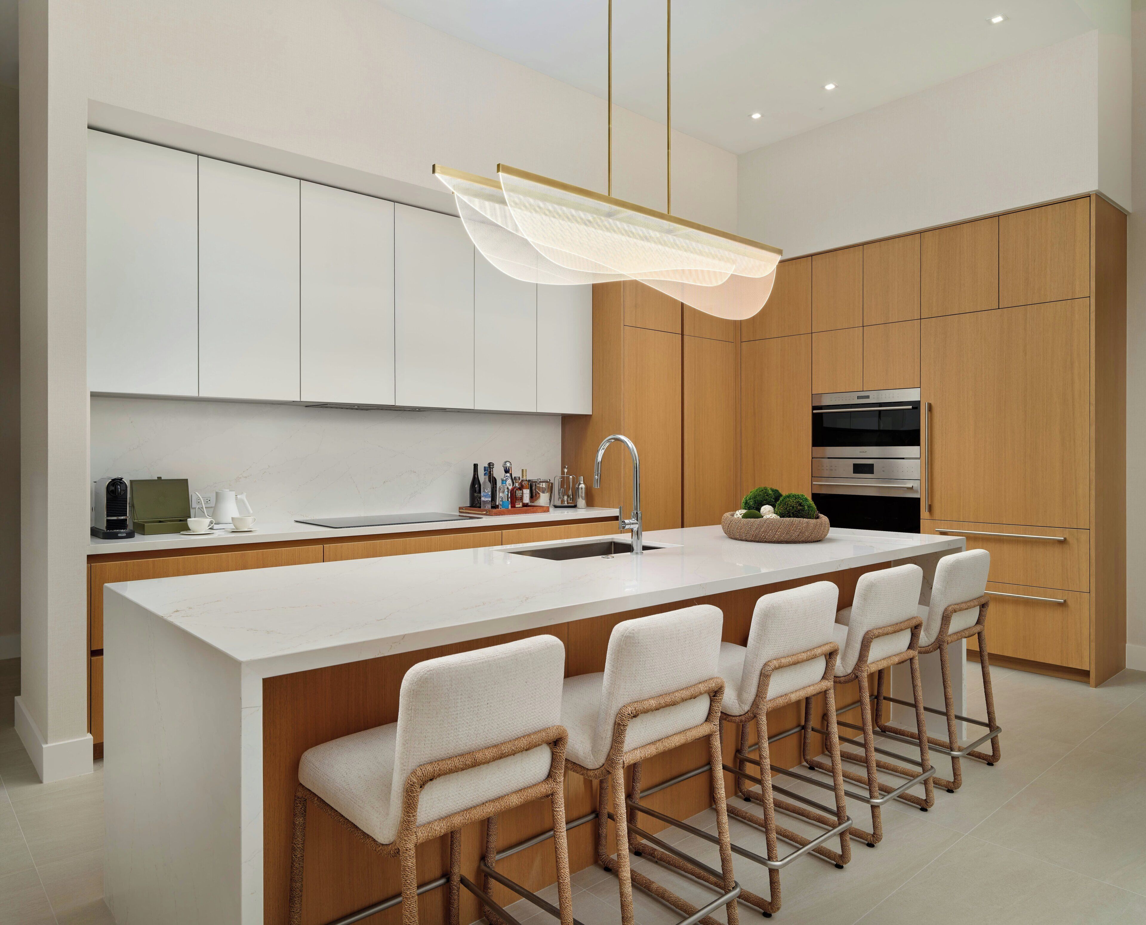 A modern kitchen with a central island, bar stools, a built-in oven, and a hanging light fixture.
