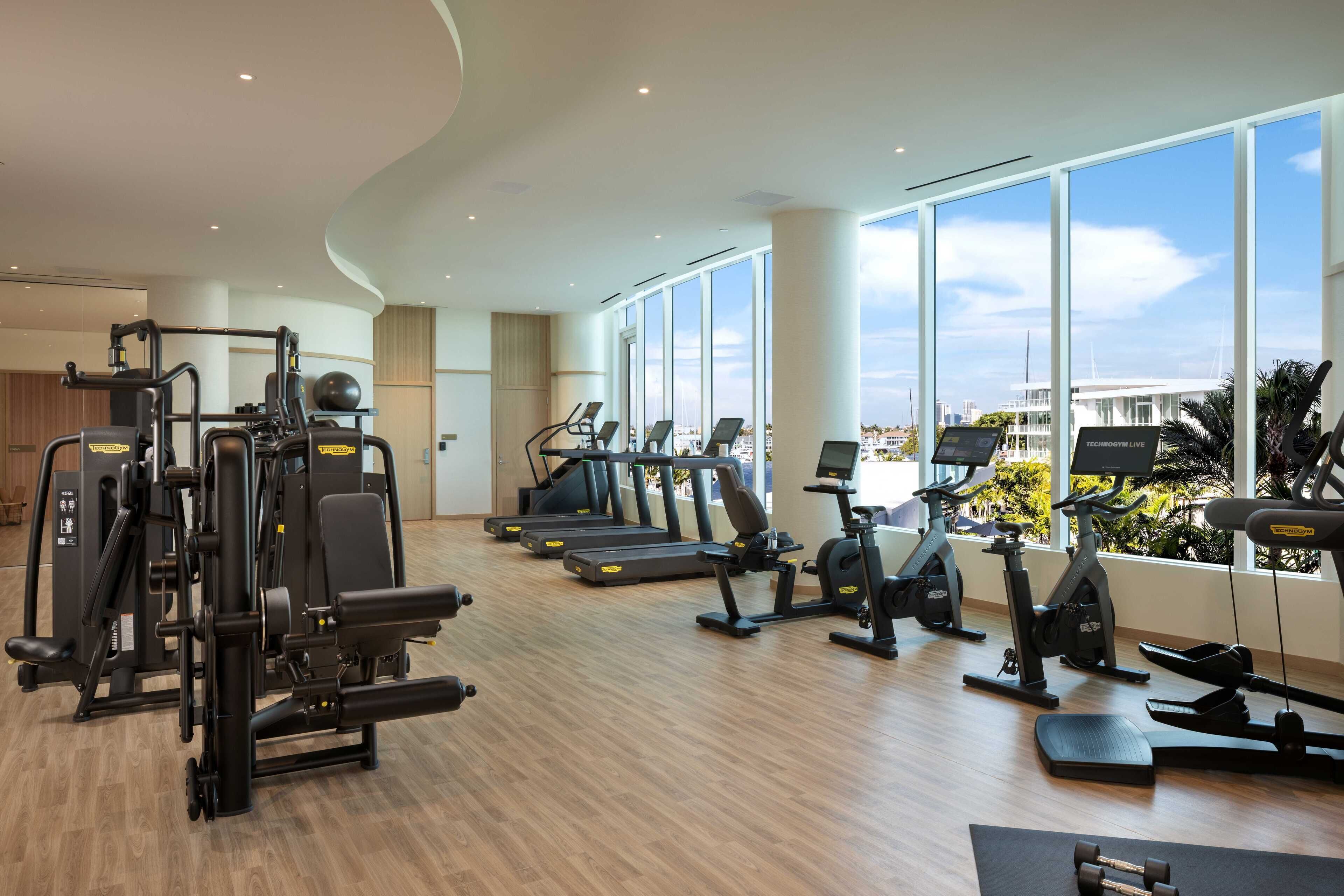 Ein modernes Fitnessstudio mit verschiedenen Trainingsgeräten, großen Fenstern und Blick auf die Stadt.