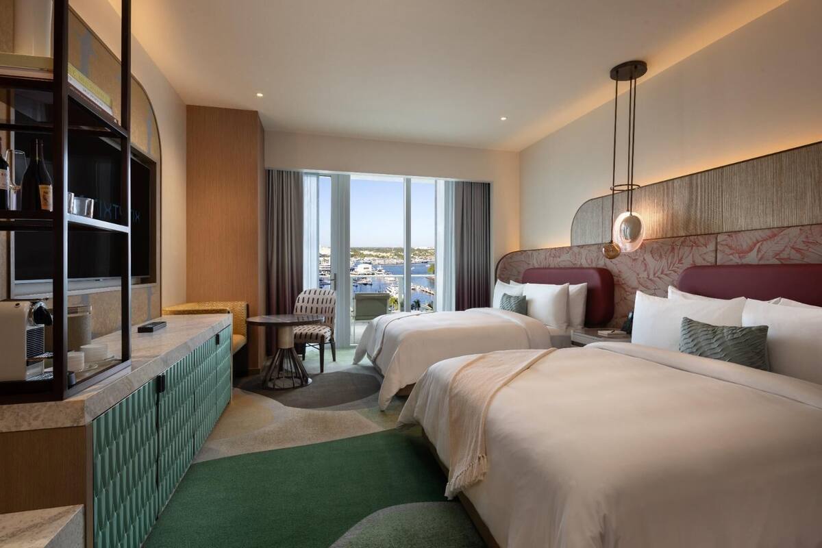 Habitación de hotel con dos camas, un minibar, un área de descanso con vistas y un ventanal grande.