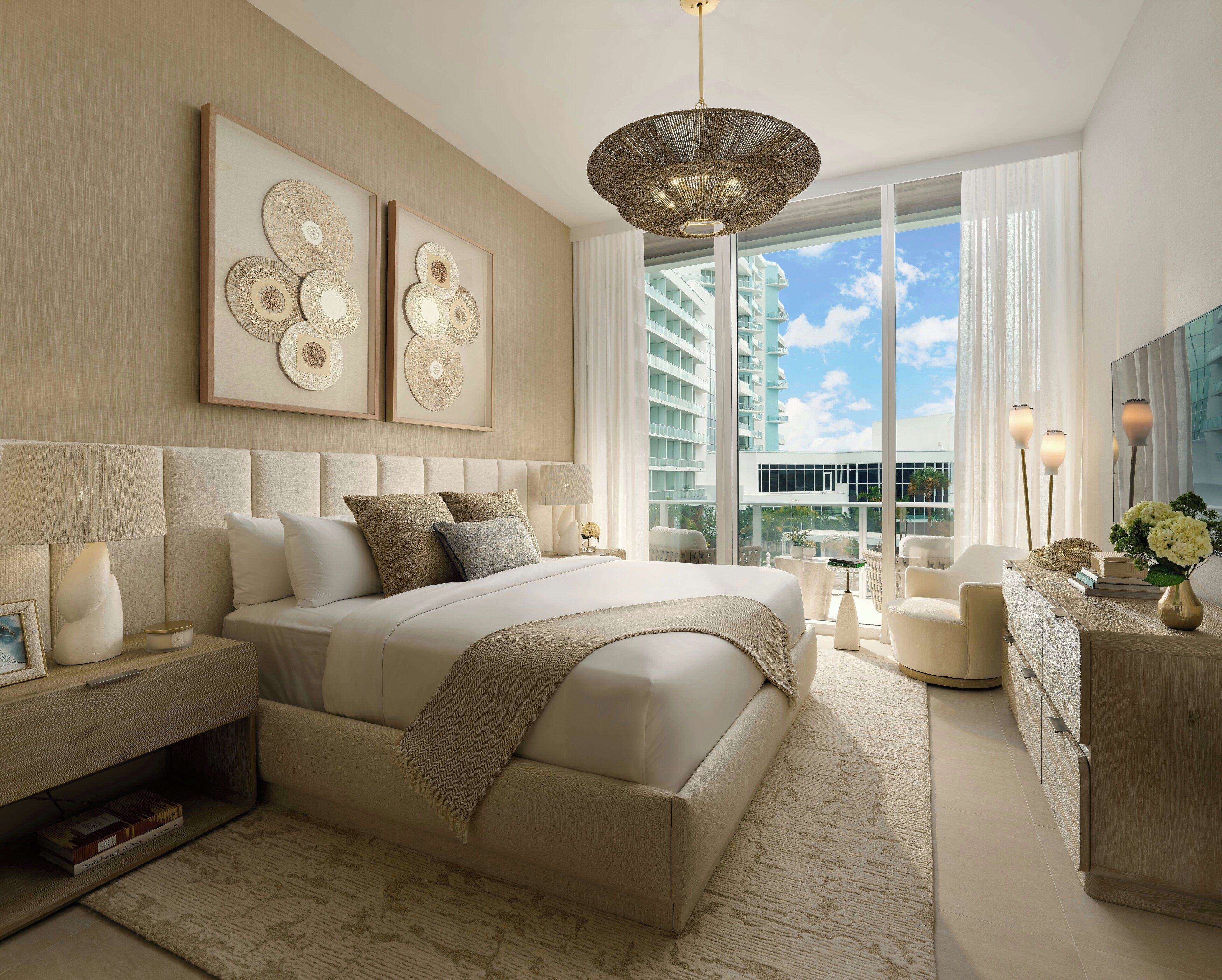 Quarto moderno com uma cama grande, mesa de cabeceira, cômoda e vista de um edifício através de janelas amplas.