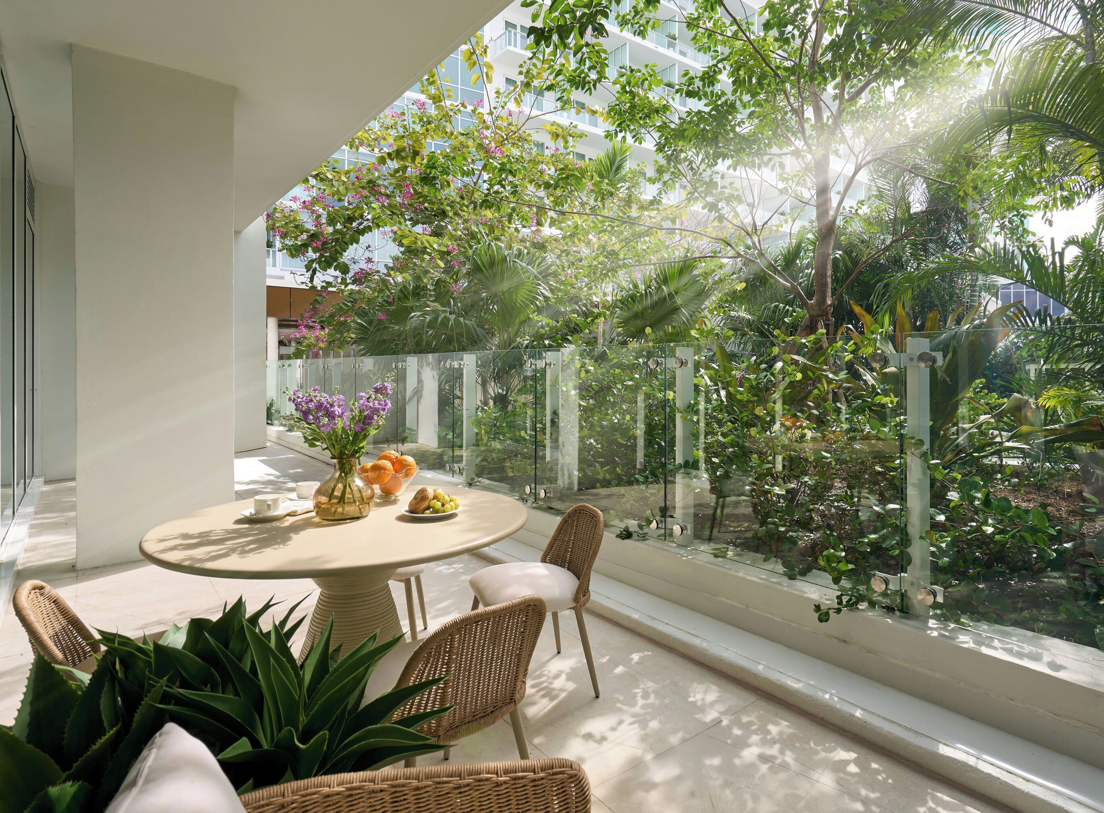 A modern outdoor seating area with a round table, wicker chairs, and a glass railing overlooking a lush garden.