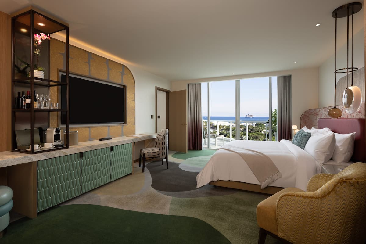 Una habitación de hotel moderna con una cama grande, un escritorio con televisor de pantalla plana, un espacio de descanso y vistas al océano.