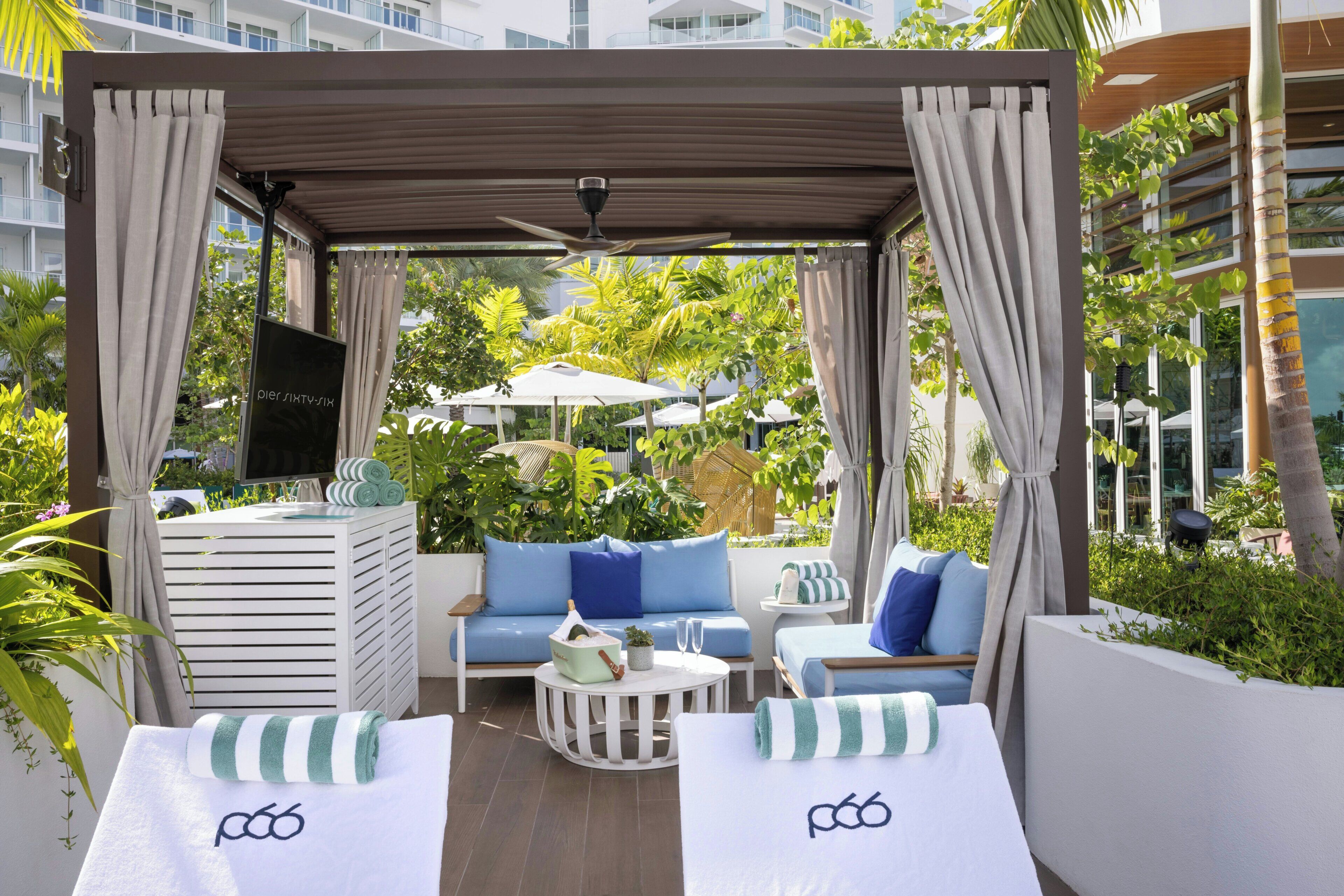 Een overdekt terras met een bank, twee fauteuils, een bijzettafeltje en een plafondventilator.