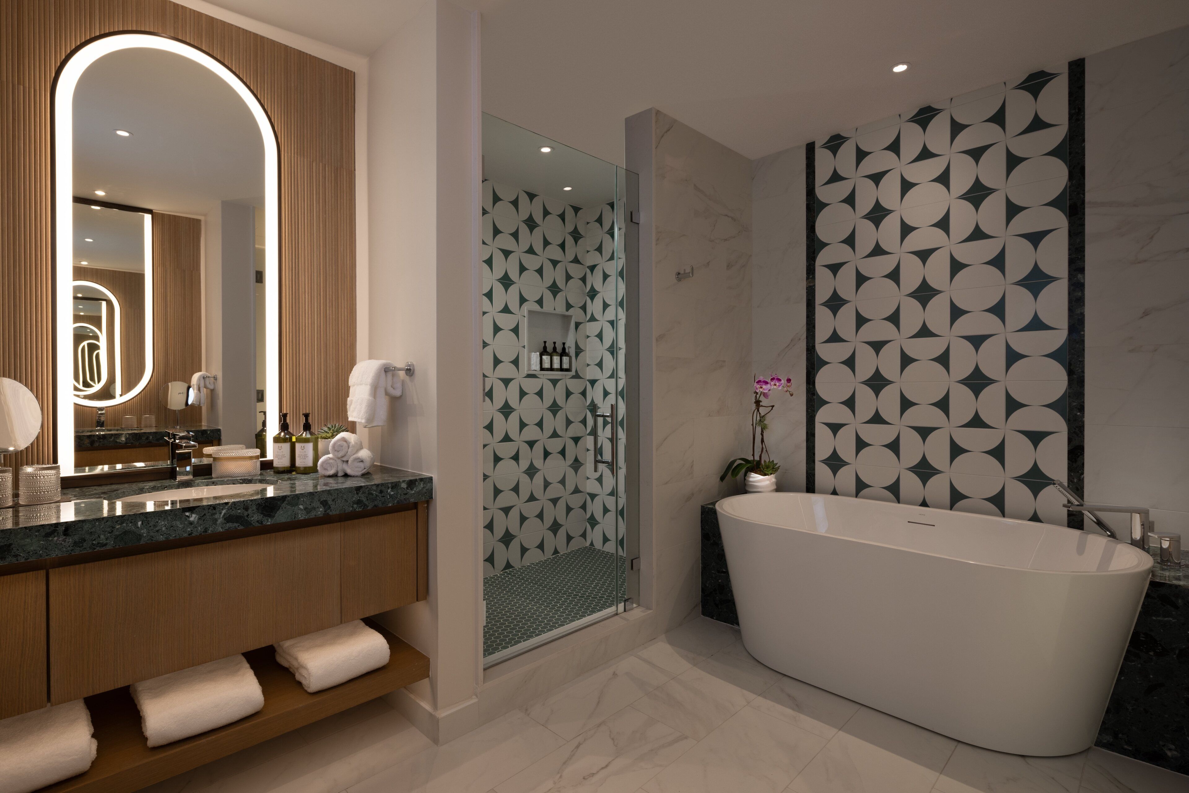 Een moderne badkamer met een vrijstaand bad, een grote spiegel en een douchegedeelte met geometrische wandtegels.