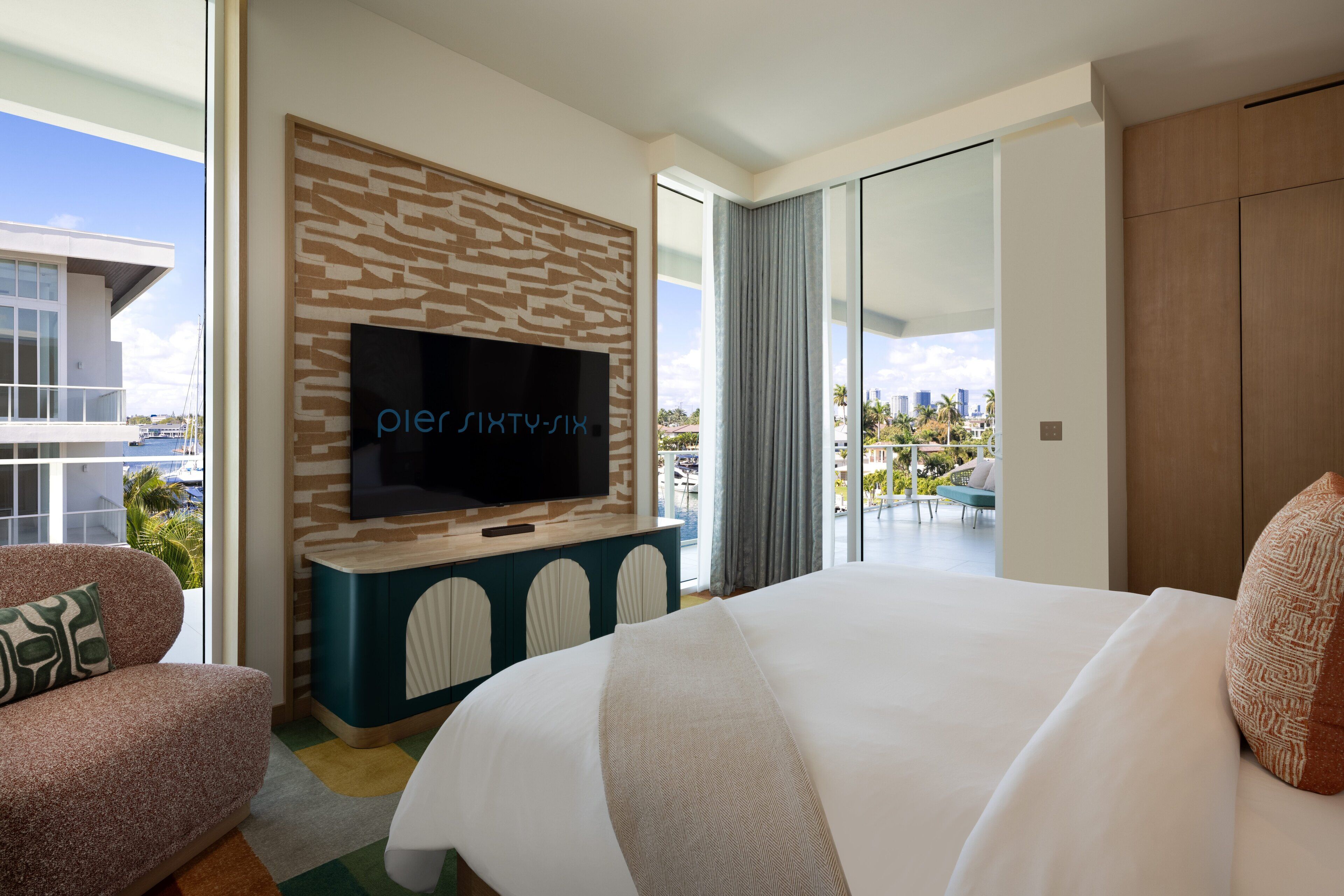 Una habitación de hotel moderna con una cama grande, un televisor instalado en la pared y un balcón con vistas a la ciudad.