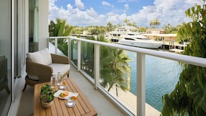 A balcony with a wicker sofa, a wooden table with a potted plant, and a view of a marina with boats and palm trees. - Pier Sixty-Six (Pier 66) (Fort Lauderdale)