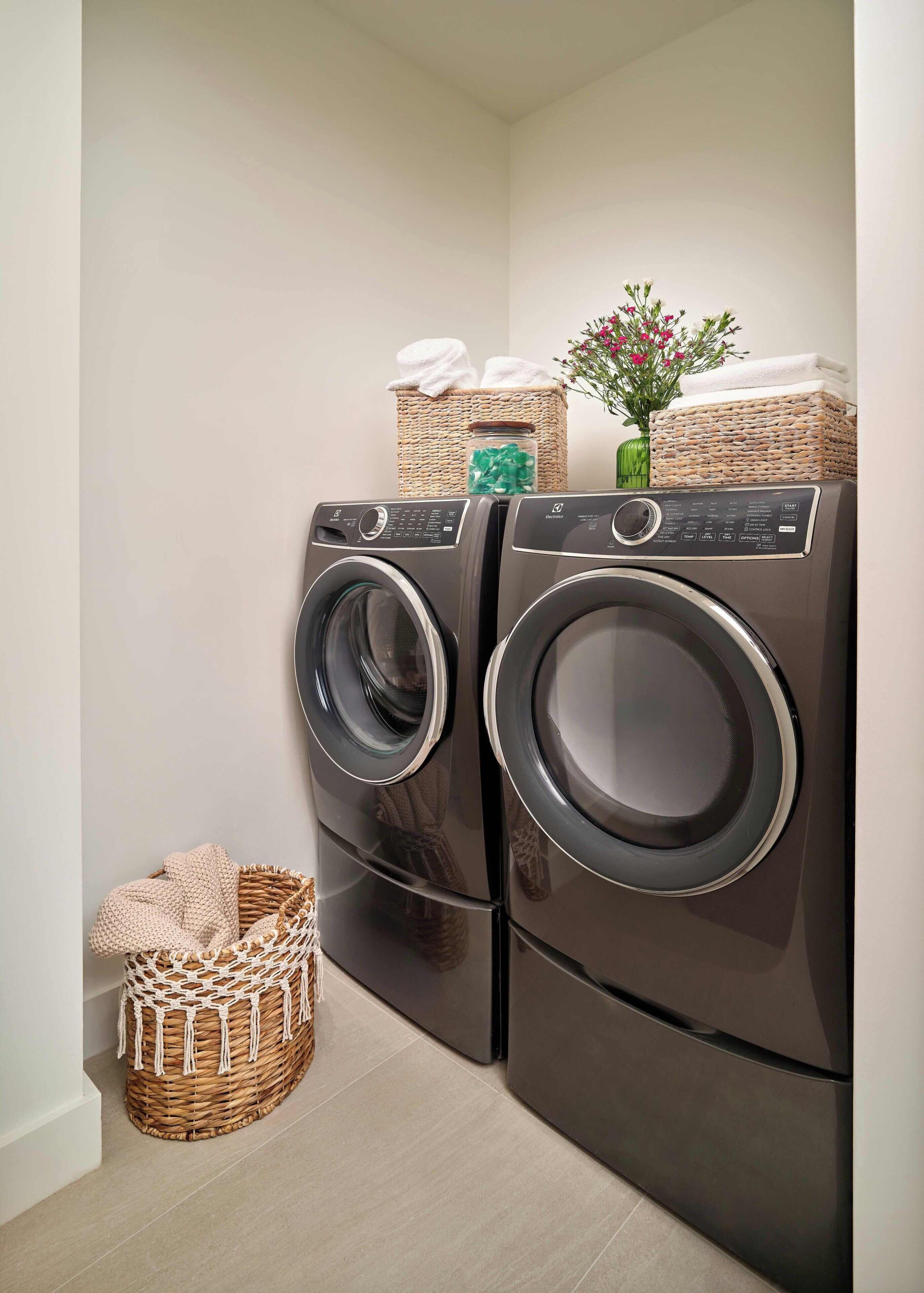 A laundry area with two front-loading washing machines, wicker baskets, and a small vase with flowers.