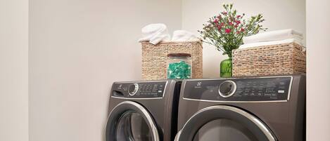 A laundry area with two front-loading washing machines, wicker baskets, and a small vase with flowers.