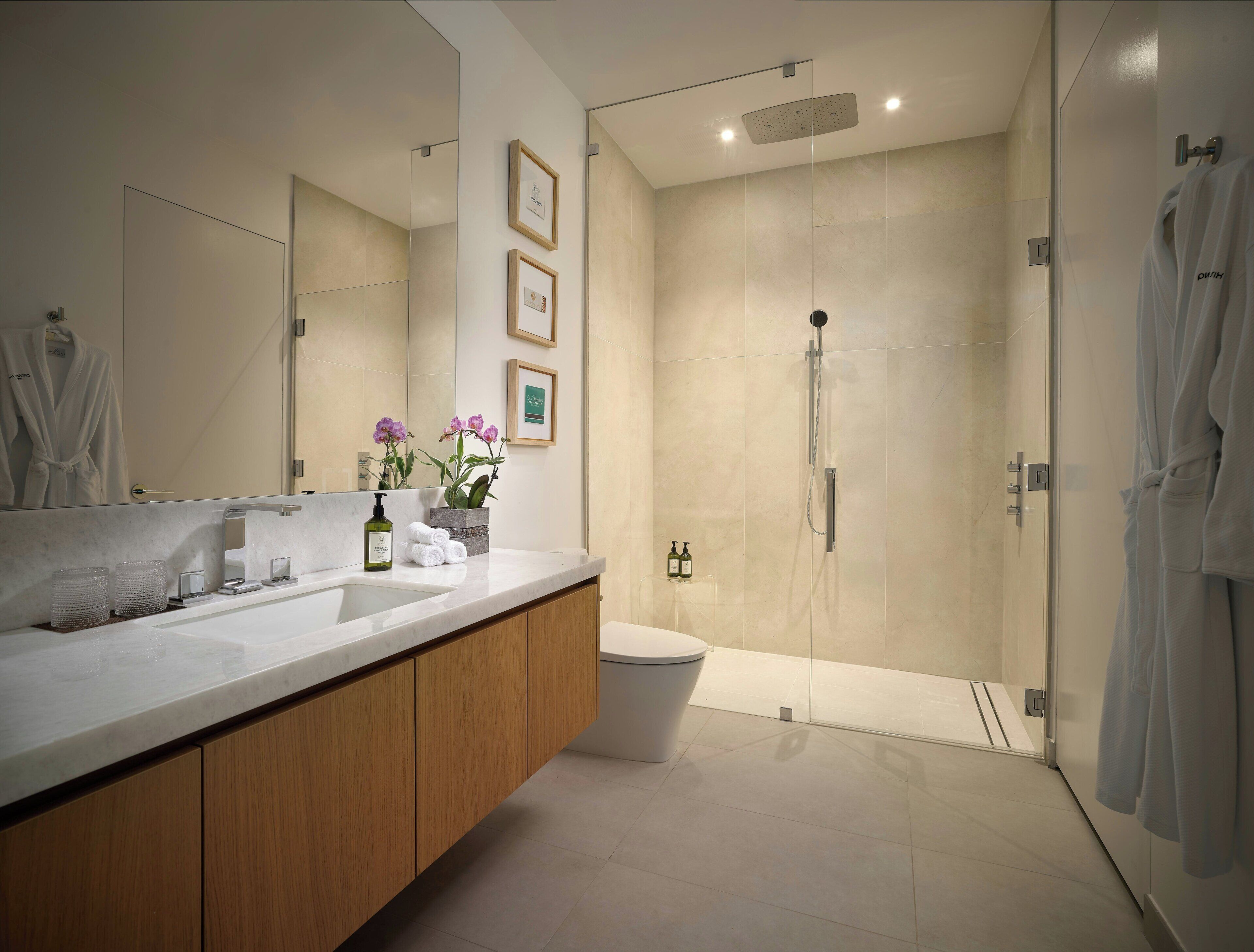 A modern bathroom with a large mirror, wooden vanity, a shower, and a toilet.