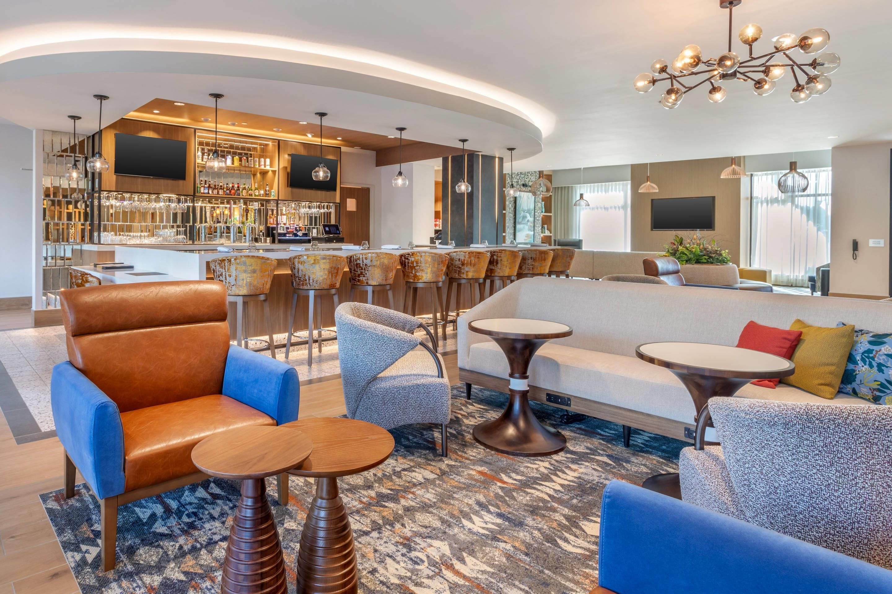Eine moderne Hotelhalle mit Barbereich, Sitzgelegenheiten und einem großen Fernsehbildschirm.