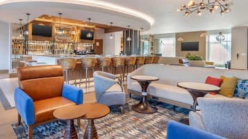 Un moderno vestíbulo de hotel con área de bar, arreglos de asientos y una gran pantalla de televisión.