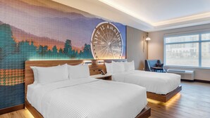 Habitación de hotel con dos camas, un mural grande en la pared, una ventana con vistas y una silla.