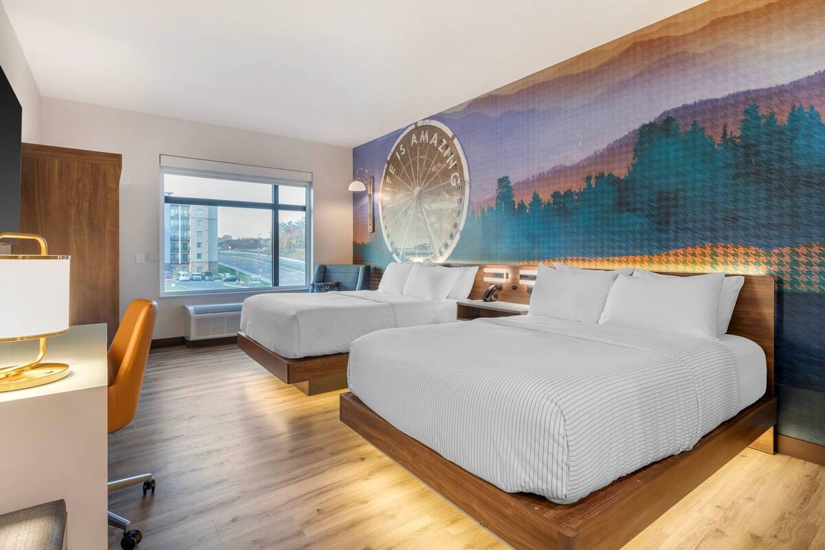 Ett hotellrum med två sängar, ett skrivbord, en stol, ett stort fönster och en väggmålning som föreställer ett pariserhjul.