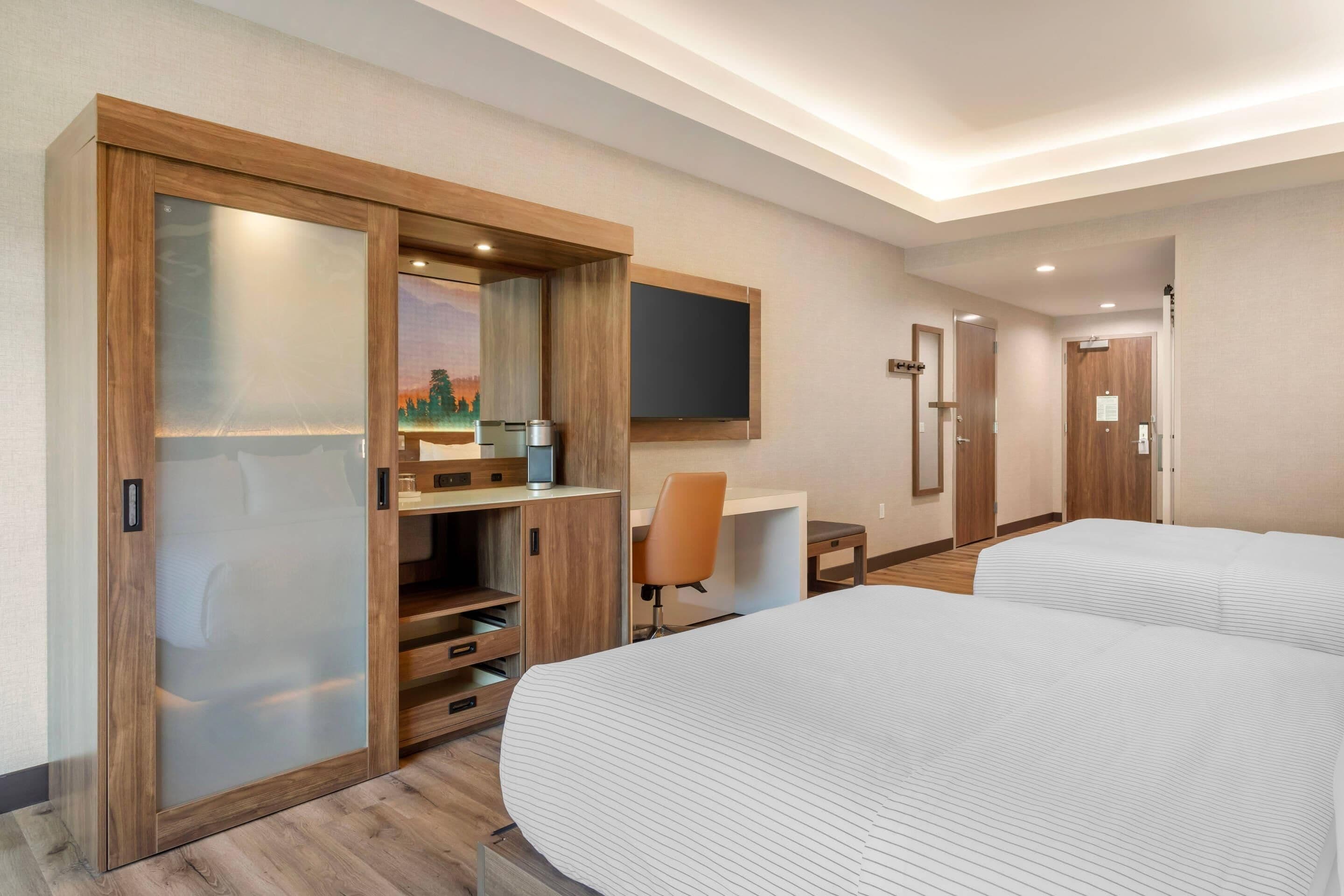 A hotel room with two beds, a desk, a chair, a wardrobe, and a TV.