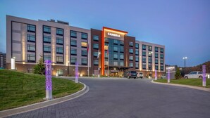 Un hotel moderno con un llamativo letrero CAMBRIA, varios pisos y una zona de estacionamiento.