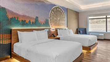 Habitación de hotel con dos camas, un mural, un ventanal y vista al estacionamiento.