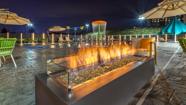Un área de piscina al aire libre con una chimenea, sillas de descanso y sombrillas.