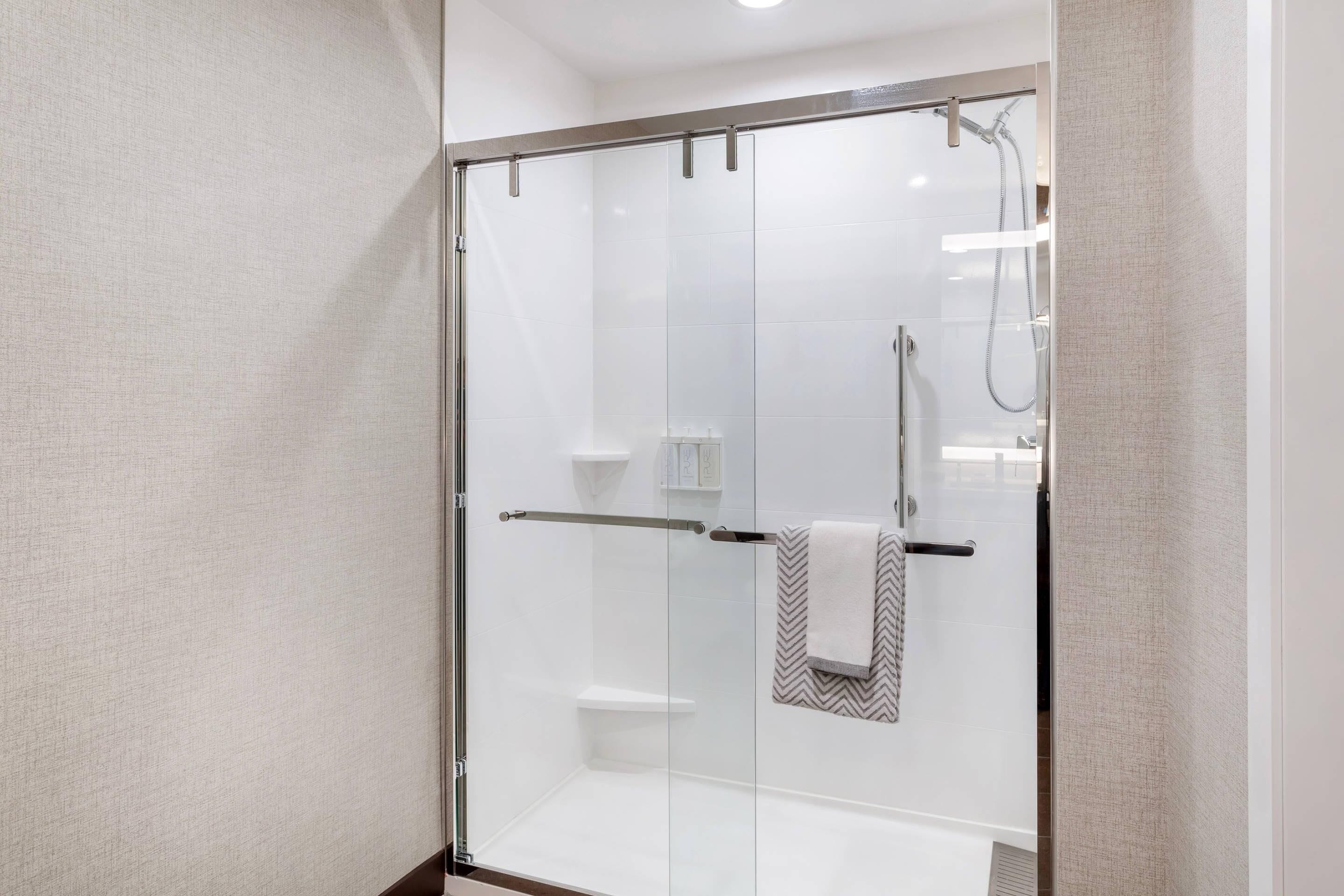 A glass-enclosed shower with a towel rack and a small shelf.