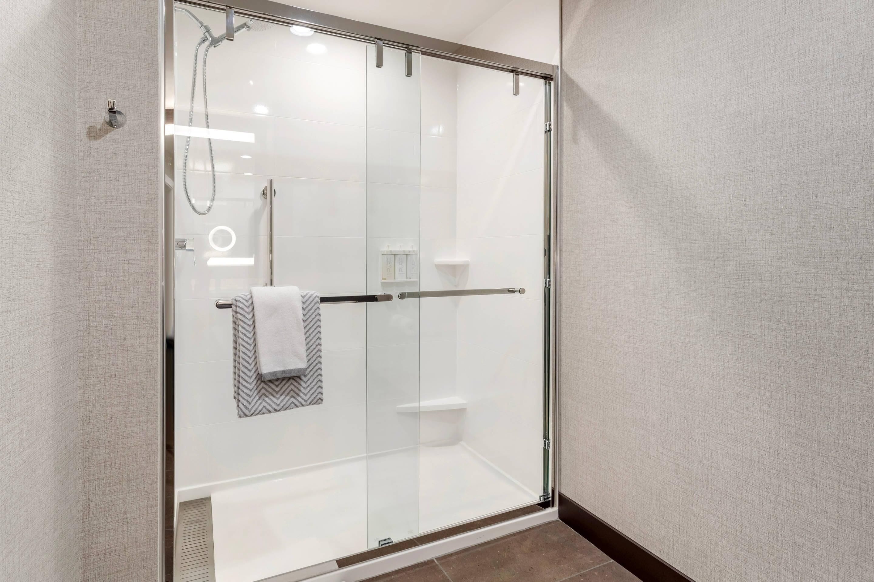 A modern shower with a glass door, a towel rack, and a soap dispenser.