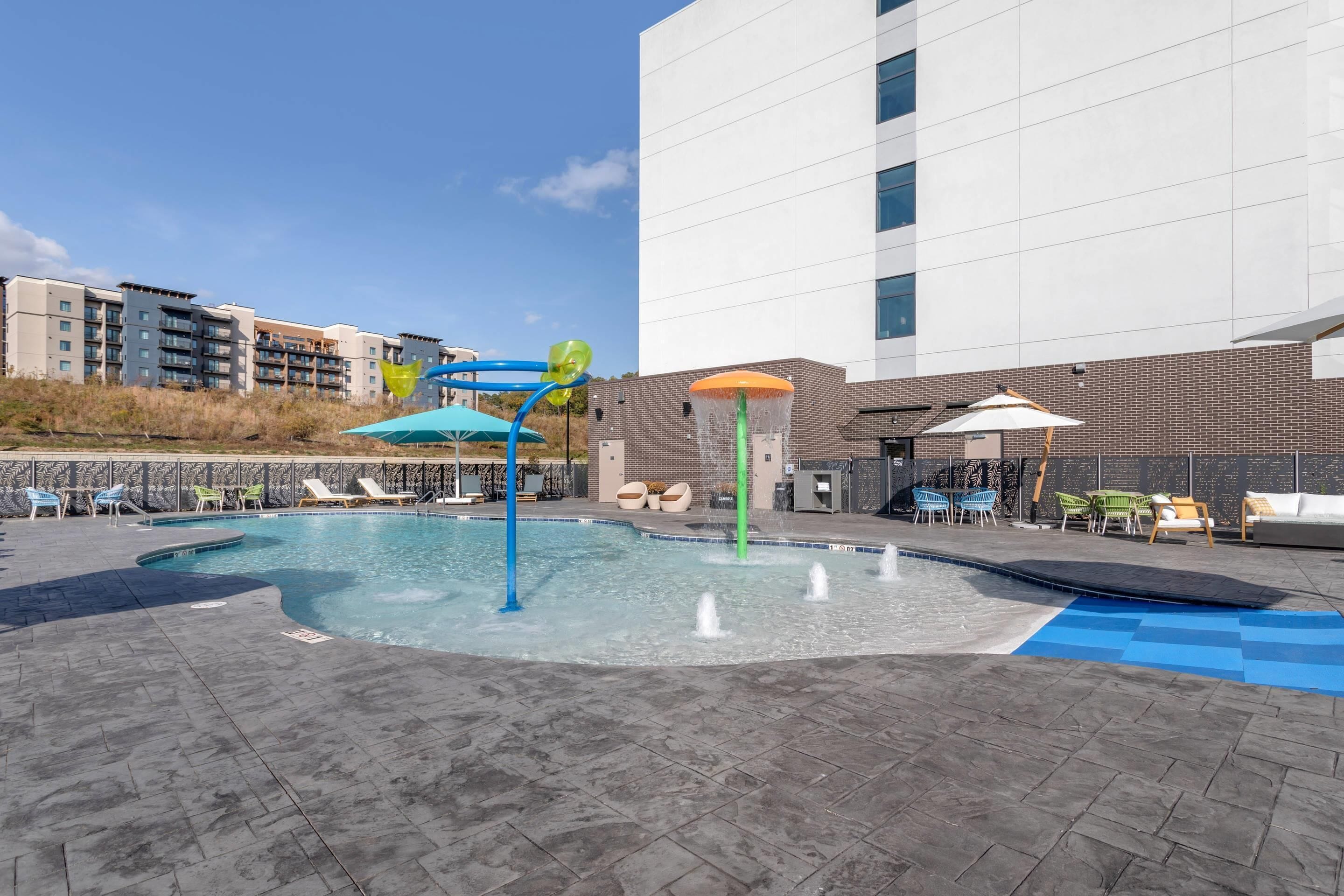 A swimming pool with water features, lounge chairs, and umbrellas.