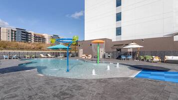 A swimming pool with water features, lounge chairs, and umbrellas.