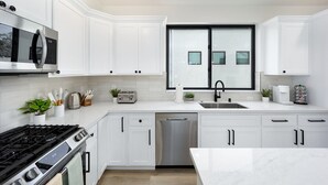 Une cuisine moderne avec des meubles blancs, des appareils en acier inoxydable et une grande fenêtre.