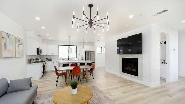 Un salon moderne avec un canapé gris, une table basse en bois et un coin repas comprenant une table blanche et des chaises orange.