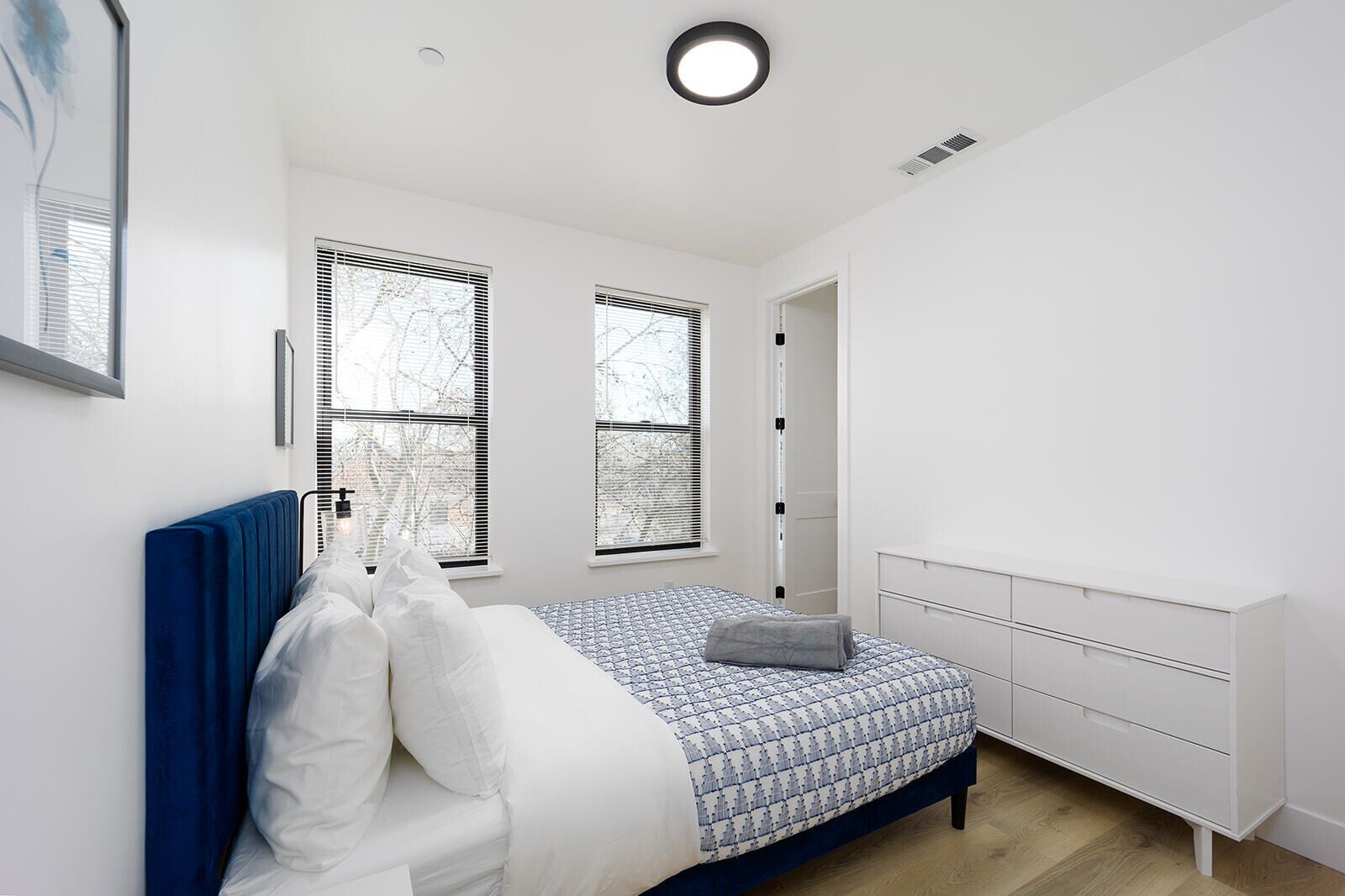 A modern bedroom with a bed, bedside table, and a window with blinds.