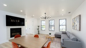 Un salon moderne avec une cheminée, un canapé gris et une table à manger avec des chaises orange.
