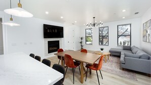 Un salon moderne avec une cheminée, un coin repas avec une table et des chaises en bois, et un canapé gris.