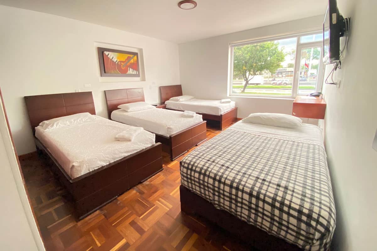 A hotel room with three beds, a large window with a view of the outside, and a painting on the wall.
